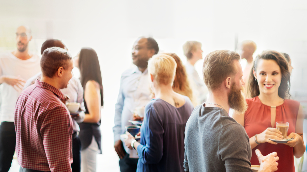 Adults talking in small groups over coffee and drinks at a bright indoor gathering