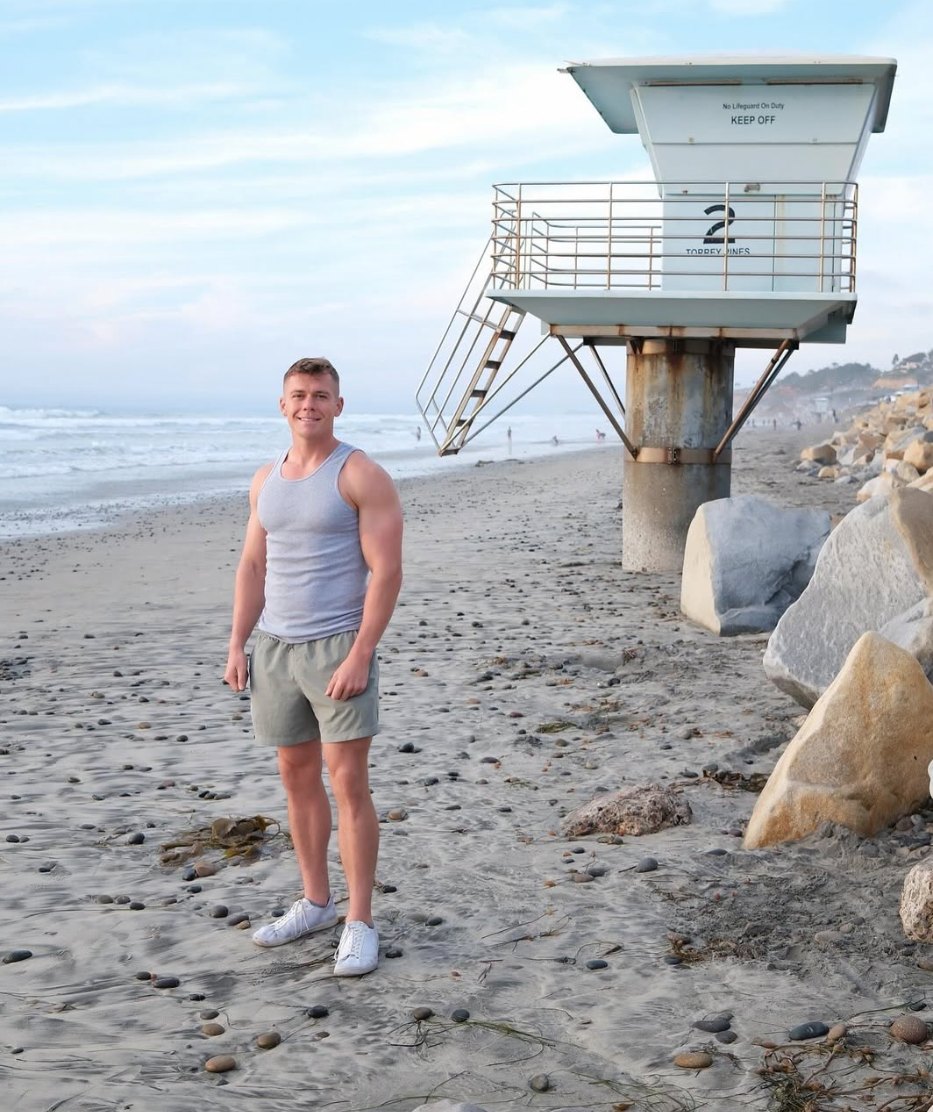 Matt Fitzsimmons standing on the beach at Torrey Pines in San Diego, smiling, with a lifeguard tower behind him.